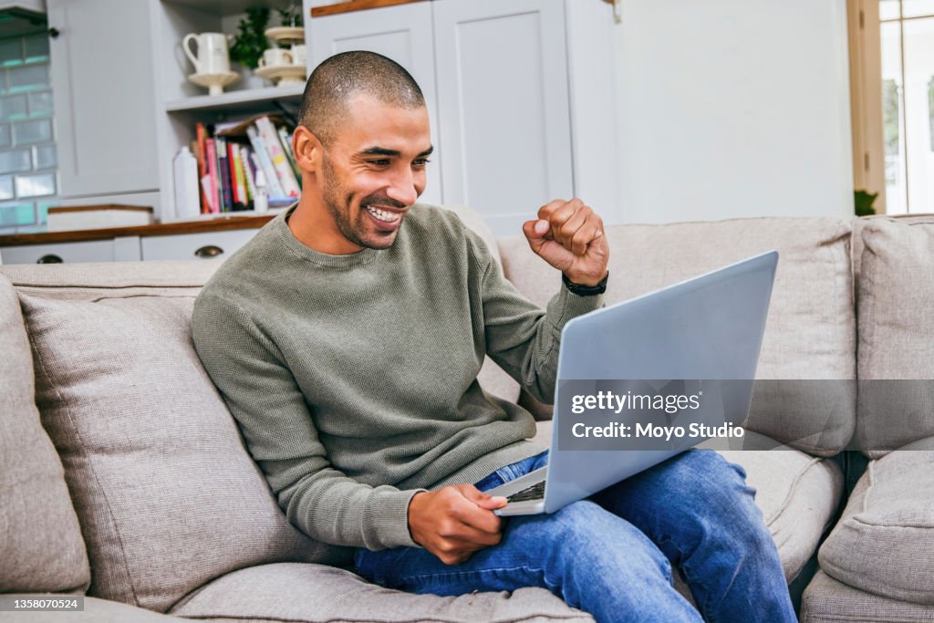 Shot of a man cheering while using his laptop to work at home