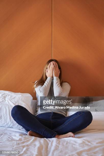 young woman sitting on bed covering her face with her hands while crying. - relationship difficulties photos stock pictures, royalty-free photos & images