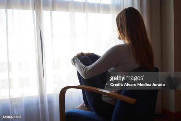 back view of a sad woman sitting in an armchair looking out the window. - unrecognizable person stock pictures, royalty-free photos & images