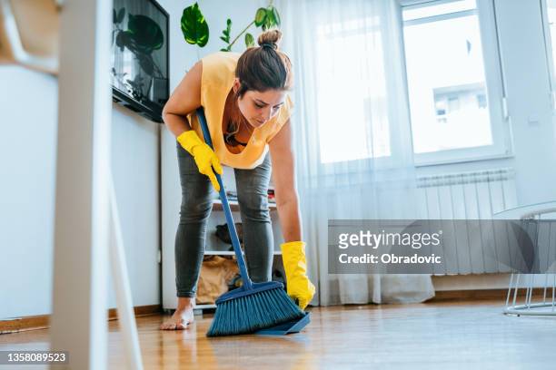 foto de una mujer usando un recogedor y barriendo el piso de su sala de estar en casa foto de archivo - barrer fotografías e imágenes de stock