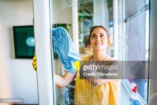 Bella giovane donna sorridente che pulisce e pulisce la finestra con flacone spray e straccio foto stock Bella giovane donna sorridente che pulisce e pulisce la finestra con flacone spray e straccio foto stock