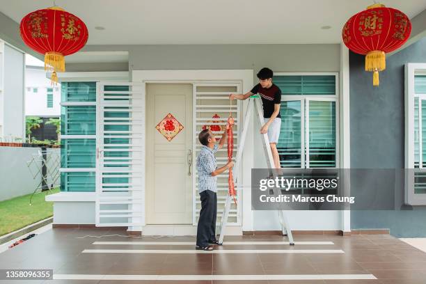 asian chinese father passing modern fire crackers lighting to son in front yard of their house during chinese new year's eve - chinese prepare for lunar new year stock pictures, royalty-free photos & images