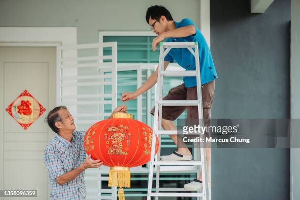 asian chinese father passing red lantern to son in front yard of their house during chinese new year's eve - 39 year old stockfoto's en -beelden