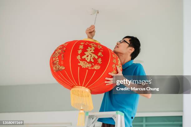 asian chinese male hanging up red lantern  in front yard of his house during chinese new year's eve - chinese lanterns stock pictures, royalty-free photos & images