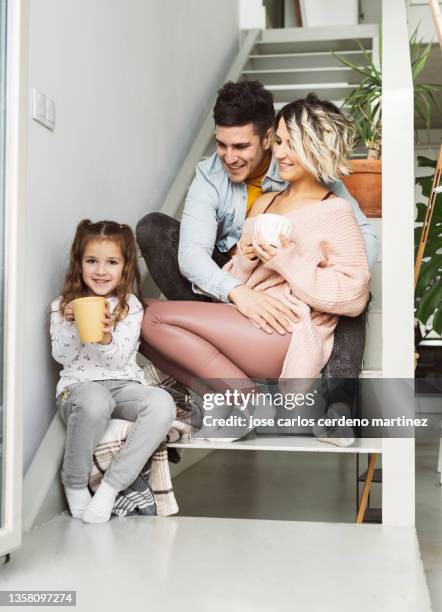 family with girls sitting at home with hot drink - family on couch with mugs stock-fotos und bilder