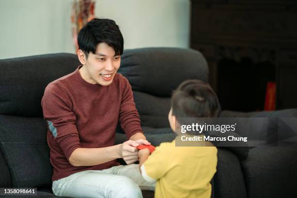 asiatische chinesische lächelnde junge männer geben dem jungen im wohnhaus während des chinesischen neujahrs einen roten umschlag - chinese new year red envelope stock-fotos und bilder