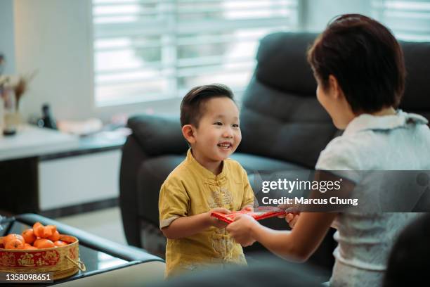 asian chinese smiling cutie boy receiving red envelope from mother at living hall during chinese new year - mom blessing son stockfoto's en -beelden