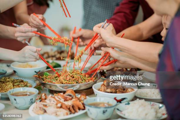 famille chinoise asiatique célébrant la veille du nouvel an chinois avec la salade crue de poisson "yusheng" pendant le dîner de retrouvailles - chinese new year food photos et images de collection