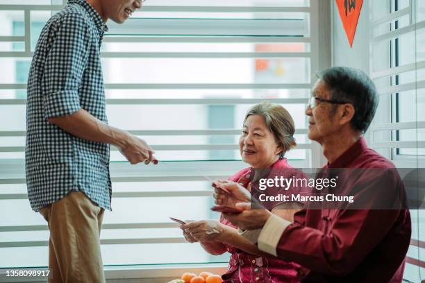 asian chinese smiling senior parent giving red envelope to their children in living hall during chinese new year - 39 year old stockfoto's en -beelden