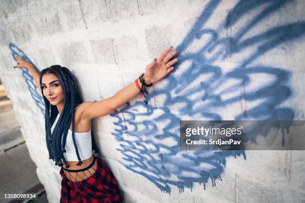rebel caucasian woman, with raised arms standing in front of the angel wings graffiti - wild wing stock pictures, royalty-free photos & images