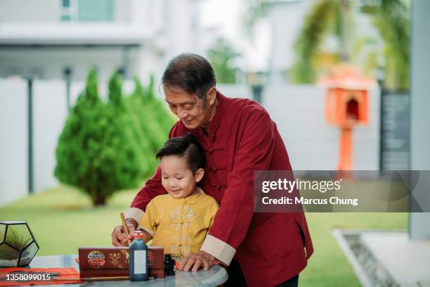 asian chinese smiling grandfather and grandson hand writing chinese calligraphy at front yard during chinese new year - 70 year male stock pictures, royalty-free photos & images