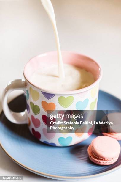 dairy free milk pouring in a cup. the cup is on a turquoise plate with two vegan macaroon on the side. - soya milk stock pictures, royalty-free photos & images