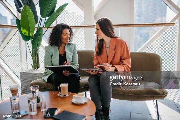 smiling colleagues sitting in the office and casually chatting while drinking coffee during a break. - two people office stock pictures, royalty-free photos & images