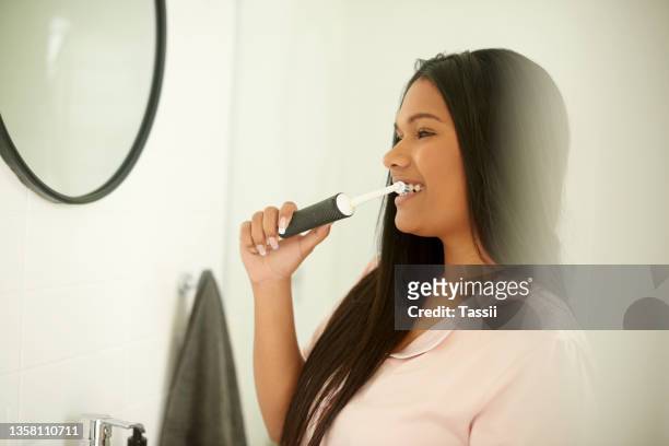shot of a young woman brushing her teeth with an electric toothbrush at home - electric toothbrush stockfoto's en -beelden