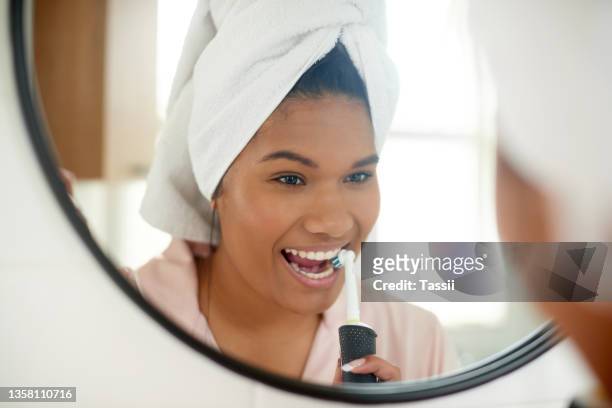 aufnahme einer jungen frau, die sich zu hause mit einer elektrischen zahnbürste die zähne putzt - zähne putzen frau stock-fotos und bilder