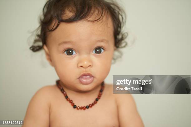 portrait of an adorable baby girl wearing a teething necklace at home - amber stockfoto's en -beelden