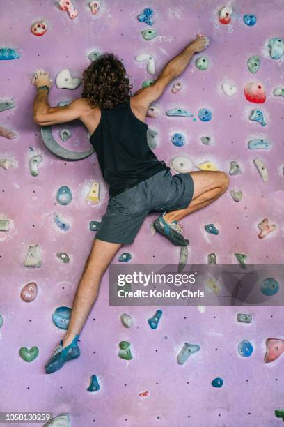 full length view of curly hair man climbing wall at gym - fake man stockfoto's en -beelden