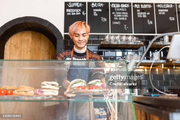 barista organizando comida recién preparada en el mostrador de exhibición de la cafetería - part time worker fotografías e imágenes de stock