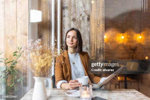 woman sitting at coffee shop with a newspaper - view-through-restaurant-window stock pictures, royalty-free photos & images