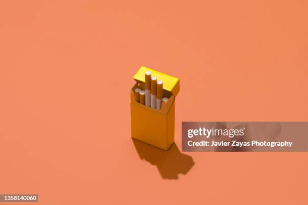 yellow cigarette pack on coral colored background - paquete de cigarrillos fotografías e imágenes de stock