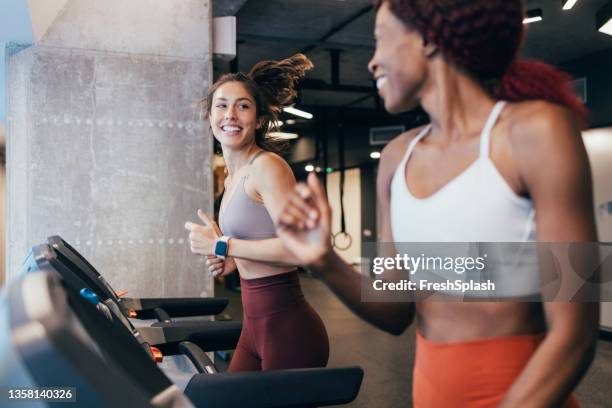 zwei motivierte sportlerinnen trainieren auf einem laufband im fitnessstudio - laufband stock-fotos und bilder