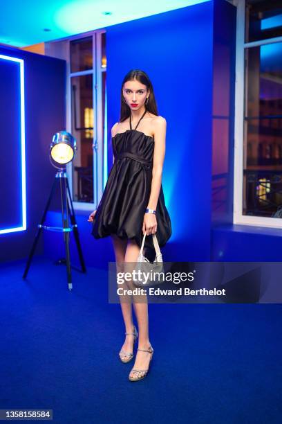 Model Diane Dagand wears earrings, a black off-shoulder gathered mini puffy party dress, a silver shiny bejeweled / studded Prada Cleo bag, bejeweled...