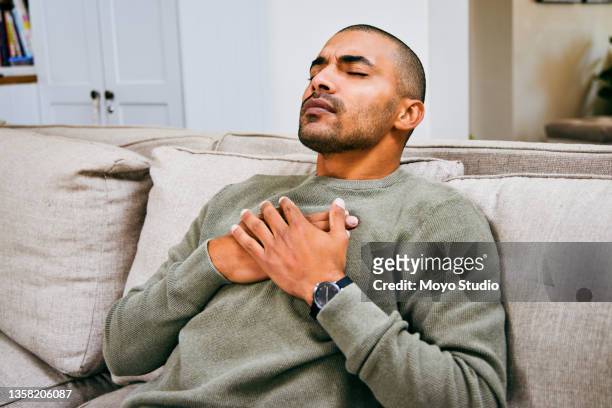 foto de un joven que experimenta dolores en el pecho en casa - ejercicios de respiración fotografías e imágenes de stock