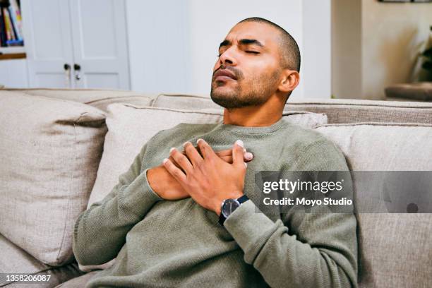 shot of a young man experiencing chest pains at home - asthma in adults stockfoto's en -beelden