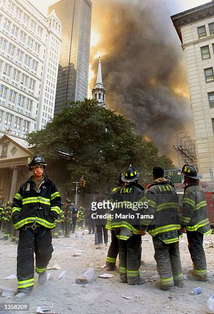 Firefighters watch as smoke rises from the site of the World Trade Center collapse September 11, 2001 in New York City after two hijacked airplanes...
