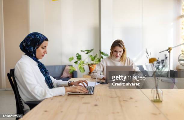 middle eastern businesswoman using laptop with a colleague sitting by at startup office - eastern european descent stockfoto's en -beelden