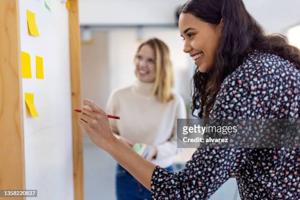 businesswoman writing her suggestion on a whiteboard during a brainstorming session at a startup company - business strategy whiteboard stock pictures, royalty-free photos & images