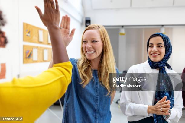 businesswomen celebrating a win with high-fives at the startup office - high five stockfoto's en -beelden