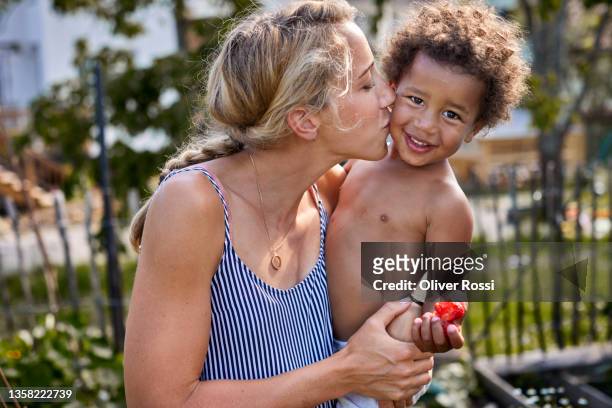mother holding and kissing happy little son in garden - diverse family stock-fotos und bilder