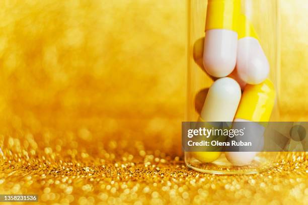white and yellow pills in glass bottle on gold glittering background. - tablettenbehälter stock-fotos und bilder