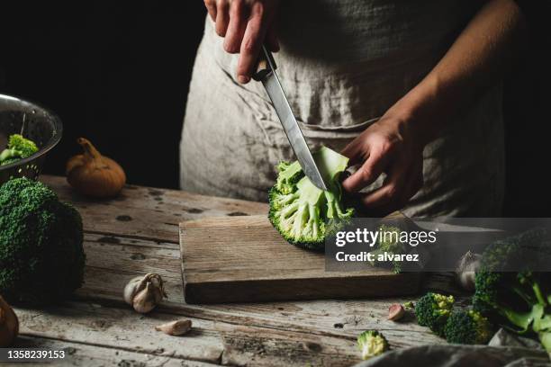 frau koch schneidet eine scheibe brokkoli auf einem hölzernen schneidebrett - brocoli stock-fotos und bilder