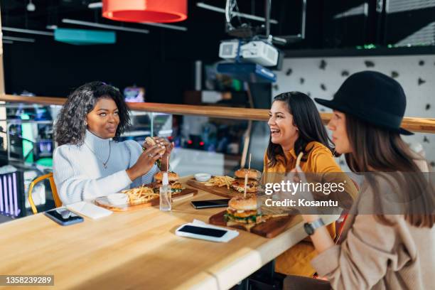 cheerful young women eating burgers and enjoying a fast food restaurant. - restaurant women friends lunch stock pictures, royalty-free photos & images