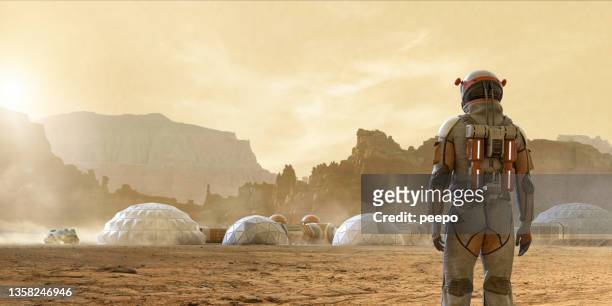 astronaut on mars looking at base camp in front of mountains - ruimtehelm stockfoto's en -beelden