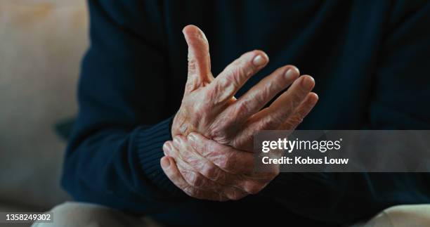 cropped shot of an unrecognisable man sitting alone at home and suffering from arthritis in his hands - arthritis stockfoto's en -beelden