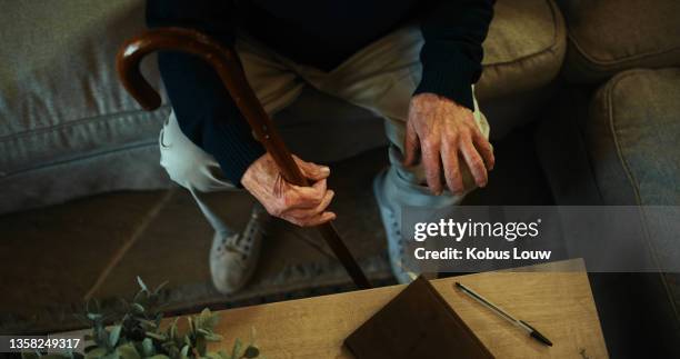 inquadratura ad alta angolazione di un uomo irriconoscibile seduto da solo sul divano di casa e con in mano il suo bastone da passeggio - bastone foto e immagini stock