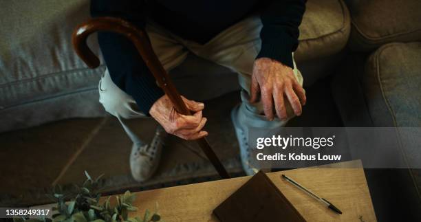 high angle shot of an unrecognisable man sitting alone on the sofa at home and holding his walking stick - wooden stick stock pictures, royalty-free photos & images