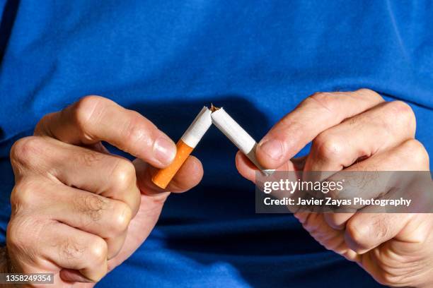 hands breaking cigarette on blue background. new year resolution. - stoppen met roken stockfoto's en -beelden