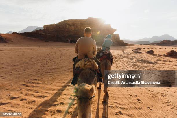 freunde, reisende, die das wadi rum erkunden wüste auf kamelen während des malerischen sonnenuntergangs - jordanien stock-fotos und bilder