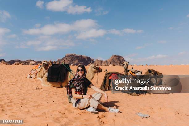 joven viajera sentada cerca de un grupo de camellos en el desierto de wadi rum - camel active fotografías e imágenes de stock