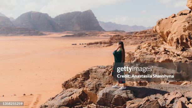 woman in dress contemplating the scenic sunset above wadi rum desert - barre stockfoto's en -beelden