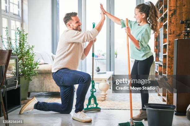 shot of a dad and daughter doing a high five while cleaning the lounge together at home - fresh deals stockfoto's en -beelden