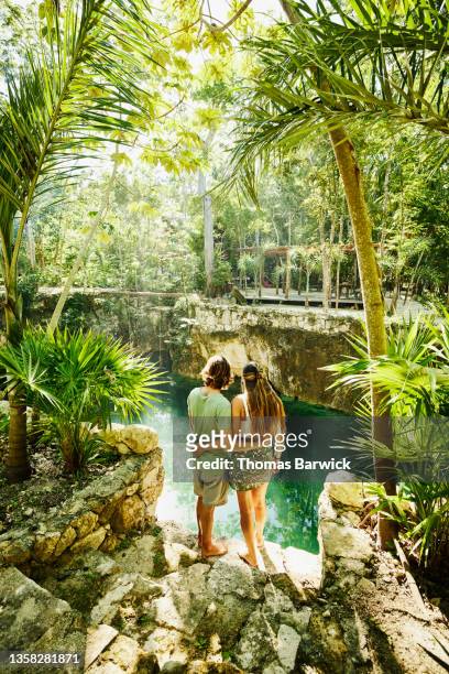 wide shot rear view of embracing couple looking at cenote while relaxing at eco resort in jungle - eco tourism foto e immagini stock