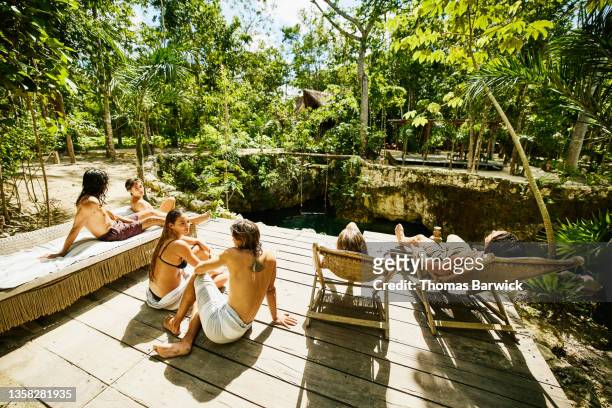 wide shot of friends hanging out in sun on platform above cenote at eco resort in jungle - eco tourism foto e immagini stock