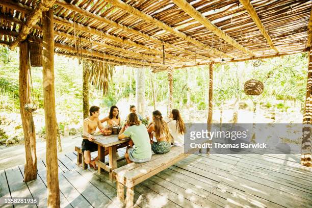 Wide shot of smiling friends sharing breakfast at eco resort in jungle
