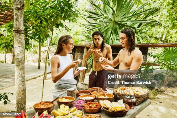 medium wide shot of friends sharing freshly made food at eco resort in jungle - alternative view stock-fotos und bilder