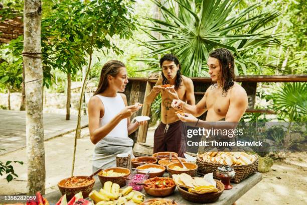 medium wide shot of friends sharing freshly made food at eco resort in jungle - eco tourism foto e immagini stock